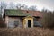 Abandoned old worn and weathered boarded wooden cottage house on grassy field.