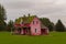 An abandoned pink color house in a green field on cloudy autumn day