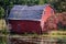 An abandoned red sinking barn sinks into a lake near Zimmerman Minnesota