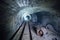 Abandoned round underground mine tunnel with remnant of equipment, pipeline and narrow-gauge railway