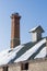 Abandoned ruin of oven chimney. Broken furnace. Snowy roof, stork slot and blue sky background in the winter.