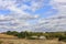 An abandoned rural house stands on the side of a rural road at the edge of a field under a cloudy sky