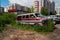 Abandoned rusting cars stand on the outskirts of a residential neighborhood, overgrown with grass against the backdrop of modern