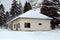 Abandoned small building surrounded with deep snow and tall trees