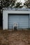 Abandoned white chair sits in a grassy area near an old garage