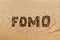 Abbreviation FOMO - fear of missing out - burnt by hand on flat wooden surface