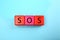 Abbreviation SOS Save Our Souls made of color cubes with letters on light blue background, top view