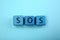 Abbreviation SOS Save Our Souls made of cubes with letters on light blue background, top view