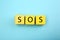 Abbreviation SOS (Save Our Souls) made of yellow cubes with letters on light blue background, top view