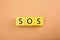 Abbreviation SOS (Save Our Souls) made of yellow cubes with letters on pale coral background, top view