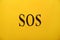 Abbreviation SOS Save Our Souls written on yellow background, top view