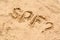 Abbreviation SPF and question mark written on sand at beach, above view