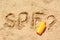 Abbreviation SPF and question mark written on sand, blank bottle of sunscreen at beach, above view