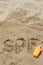 Abbreviation SPF and question mark written on sand, blank bottle of sunscreen at beach, above view. Space for text