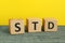 Abbreviation STD made with cubes on wooden table against yellow background