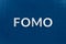 The abbreviation word fomo - fear of missing out - laid with silver letters on classic blue color flat surface