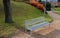 Above the ornamental pond in the park are several gray metal transparent benches on the park gravel sidewalk. autumn leaves lying