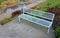 Above the ornamental pond in the park are several gray metal transparent benches on the park gravel sidewalk. autumn leaves lying