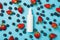 Above photo of strawberries blueberries water drops and white bottle of spray in the middle isolated on the blue background