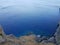 From above shot of clean blue water of calm sea near rough stony cliff on sunny day in beautiful nature.