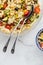 Above view of a pasta salad with long metal salad servers. Copy space below.