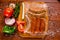 Above view of sausages inside of a plastic bags and vegetables, tomato, garlic, green pepper and onion and rosemary