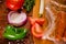 Above view of sausages inside of a plastic bags and vegetables, tomato, garlic, green pepper and onion and rosemary