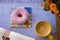 Above view of sweet pink frosted donut on the wooden table, coffee cup and orange flowers - pause or breakfast with a book