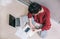 Above view of young brunette woman using laptop managing domestic budget alone, making notes with pencil, sitting on the floor