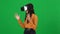 Absorbed African American teenage girl in VR headset pointing around turning on green screen. Portrait of excited female