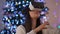 Absorbed Asian woman in VR headset gaming online at background of Christmas light on New year's eve. Front view