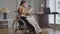 Absorbed young paraplegic woman in wheelchair reading book drinking coffee in the morning at home indoors. Portrait of