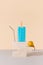 Abstract arrangement of metal straw, cooler pack popsicle and pear on marble blocks against beige and gray background.