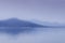 An abstract blue blurry seascape with two mountain rages and water foreground.