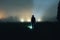 An abstract blurry grainy edit of a spooky hooded figure silhouetted on a foggy night in a field. With a dark, eerie atmosphere