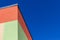 An abstract fragment of a green and orange building combined with a bright blue sky.