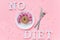 Abstract funny face of woman from donut with eyes and hair from centimeter tape on plate, cutlery and text No diet on pink