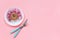 Abstract funny face of woman made donut with eyes and hair from centimeter tape on plate, cutlery on pink background. Fast food,