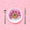 Abstract funny face of woman made donut with eyes and hair from centimeter tape on plate, cutlery on pink background. Fast food,