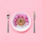 Abstract funny face of woman made donut with eyes and hair from centimeter tape on plate, cutlery on pink background. Fast food,