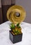 abstract golden circular sculpture with a small black vase of succulent plant, on top of a marbled table.