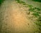 Abstract high contrast close-up of rocky gravel driveway road tire imprint in brown sand with grass areas in background