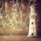 Abstract nautical lifestyle concept. old vintage lighthouse on wooden table and warm gold garland lights. vintage filtered image