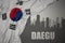 Abstract silhouette of the city with text Daegu near waving national flag of south korea on a gray background