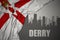 Abstract silhouette of the city with text Derry near waving national flag of northern ireland on a gray background