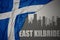 Abstract silhouette of the city with text East Kilbride near waving national flag of scotland on a gray background
