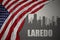 Abstract silhouette of the city with text Laredo near waving national flag of united states of america on a gray background. 3D