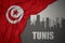 Abstract silhouette of the city with text Tunis near waving colorful national flag of tunisia on a gray background