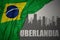 Abstract silhouette of the city with text Uberlandia near waving national flag of brazil on a gray background