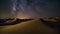 Abstract time lapse night sky with shooting stars over desert dune landscape. Milky way glowing lights background.